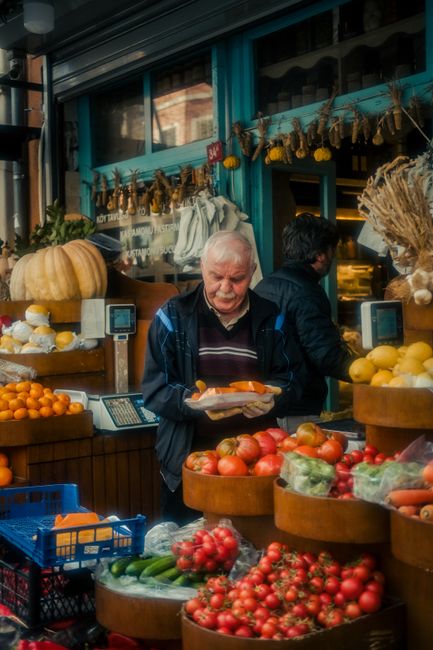 An elderly man shopping for fresh produce at a vibrant outdoor market stall filled with vegetables and fruits.